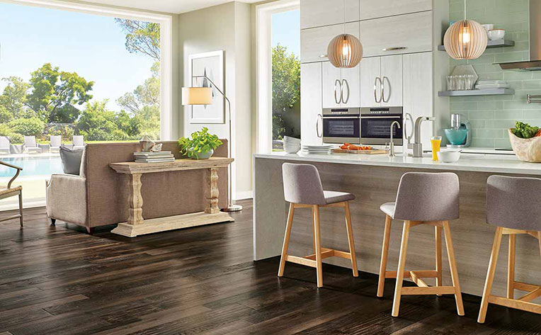 Open kitchen and living room with bar seating, decorative lighting, and luxury vinyl plank flooring with a large bay window that looks out to a backyard pool.